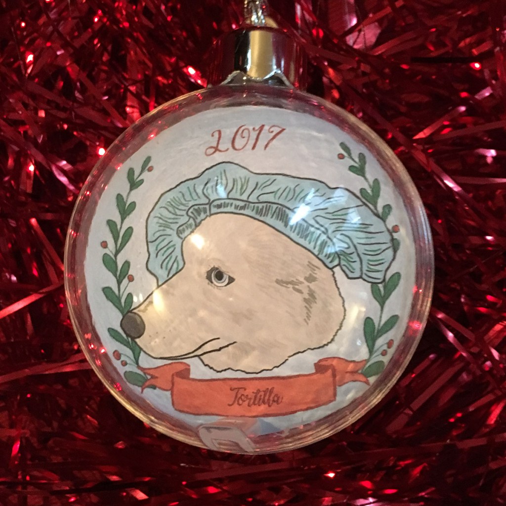 Holiday ornament with an illustrated portrait of a dog named Tortilla wearing a funny hat