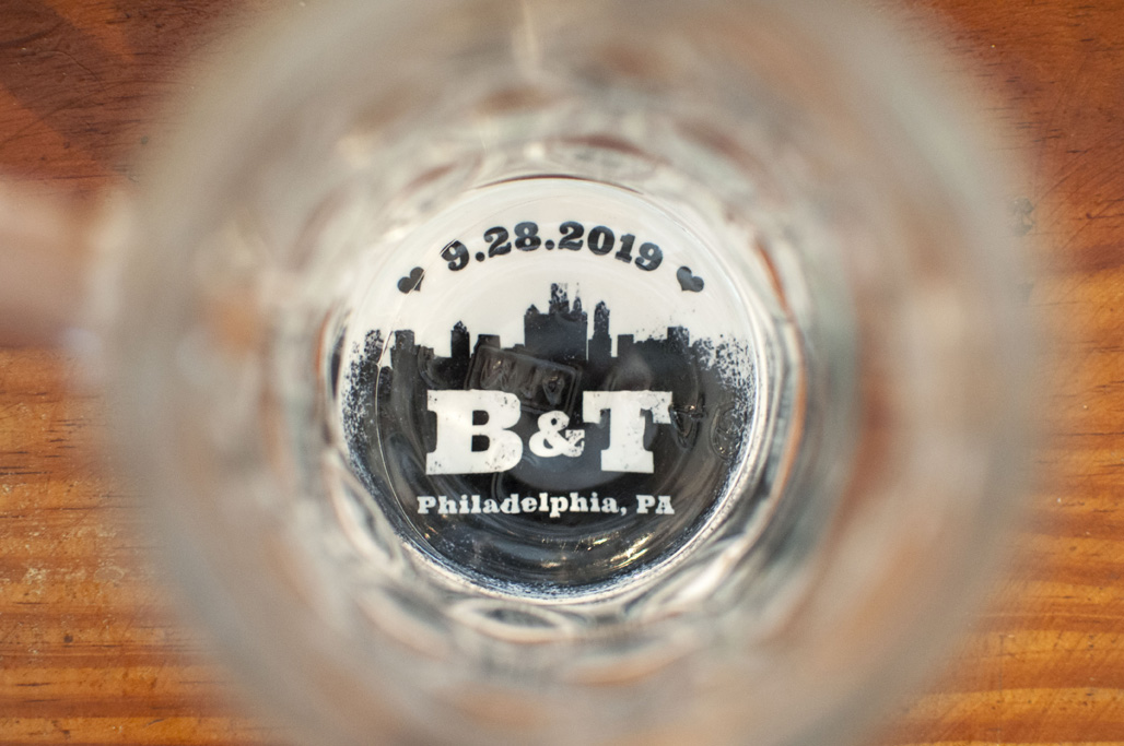 Looking through a beer mug, a coaster with a spray paint design that features the Philadelphia skyline and reads 9.28.2019 B&T Philadelphia, PA