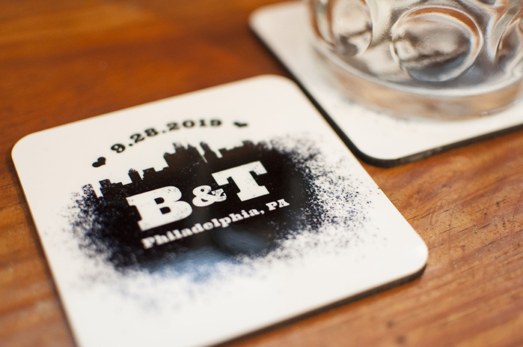 A beer mug next to a coaster with a spray paint design that features the Philadelphia skyline and reads 9.28.2019 B&T Philadelphia, PA